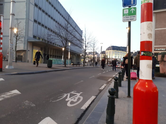People walking along a street with bike lanes and urban infrastructure near Brussels Central Station at dusk leading a Happy life