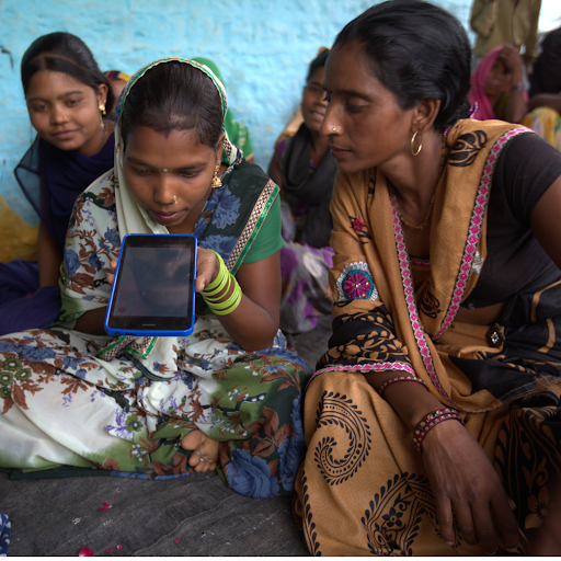 Rural Indian women learning to use a digital tablet during a community training session.