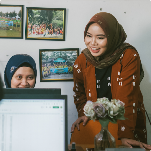 Two women in a professional setting, working on laptops with framed photos in the background.