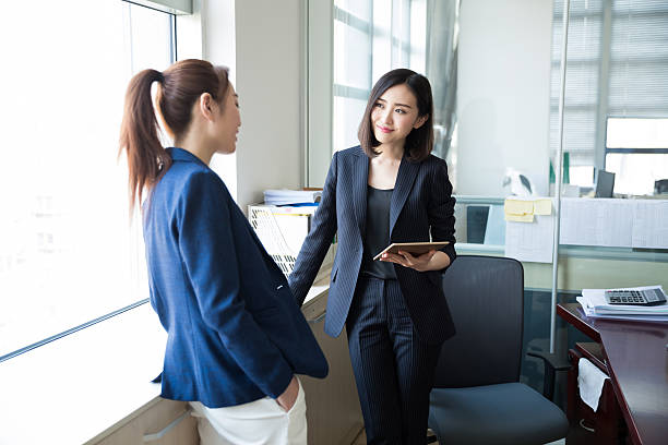 Two female executives in formal suits having a discussion in the office window showing women empowerment
