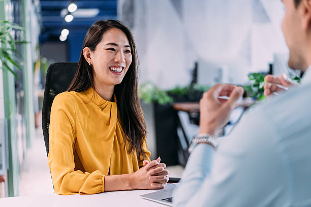 A smiling woman in a yellow blouse speaking during a professional meeting at her desk. Showing women empowerment.