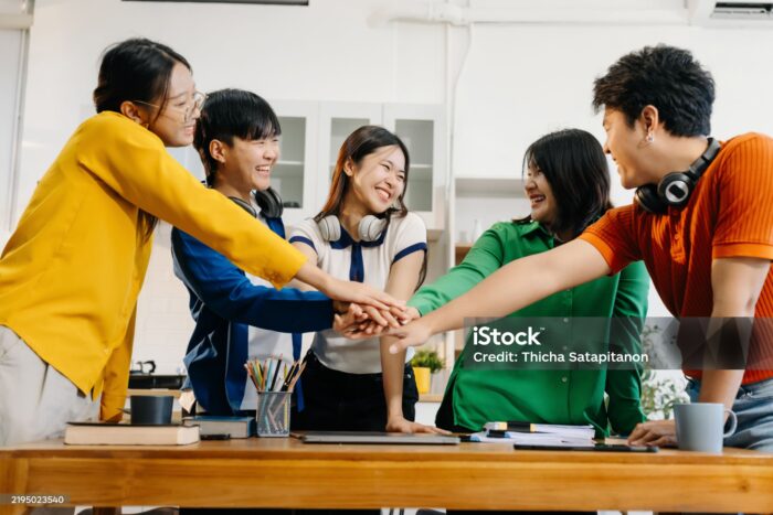 A diverse group of young professionals putting hands together in a cheerful team-building moment with women empowerment.