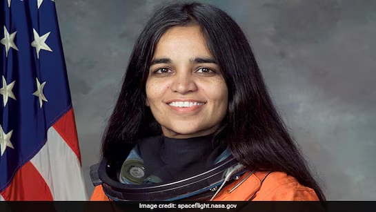 Portrait of woman empowerment astronaut Kalpana Chawla wearing a space suit, standing in front of the American flag.